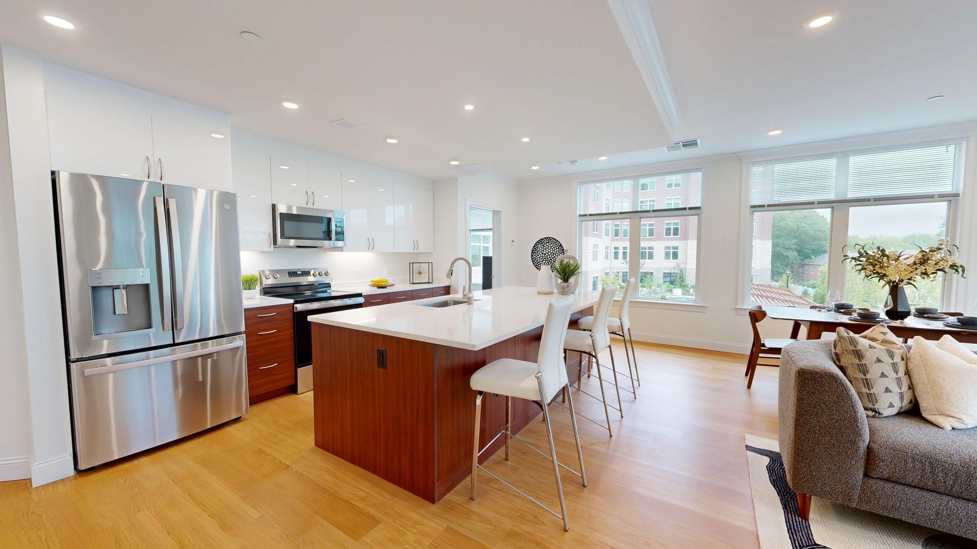 A bright, open-concept kitchen with a large wooden island, white countertops, stainless appliances, and wooden floors.