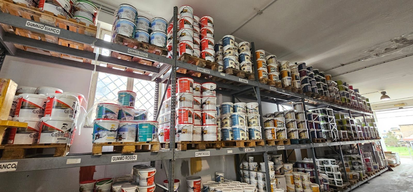 Scaffali pieni di barattoli di vernice all'interno di un magazzino, una finestra visibile.