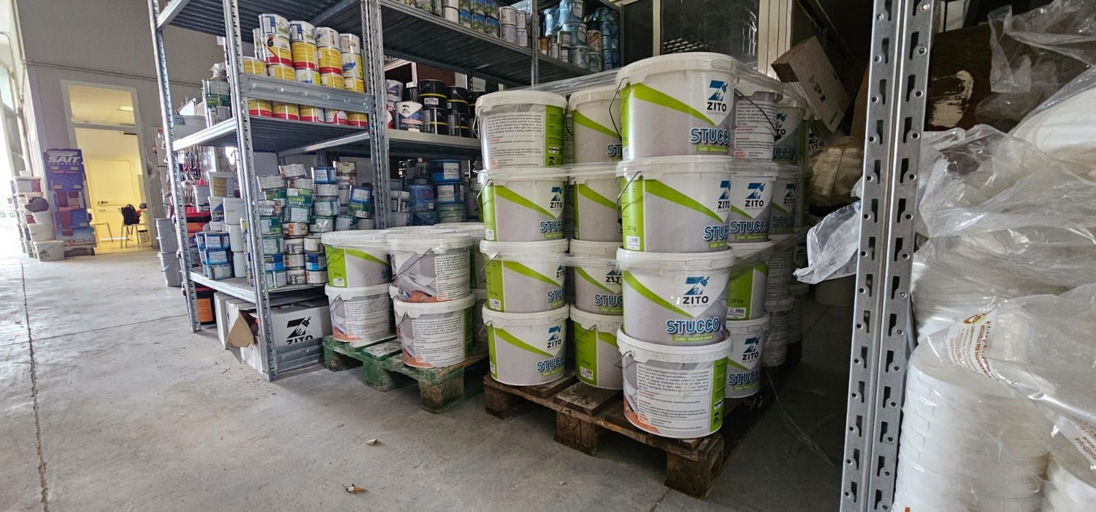 Interno di un magazzino con scaffali pieni di barattoli di vernice e secchi impilati.