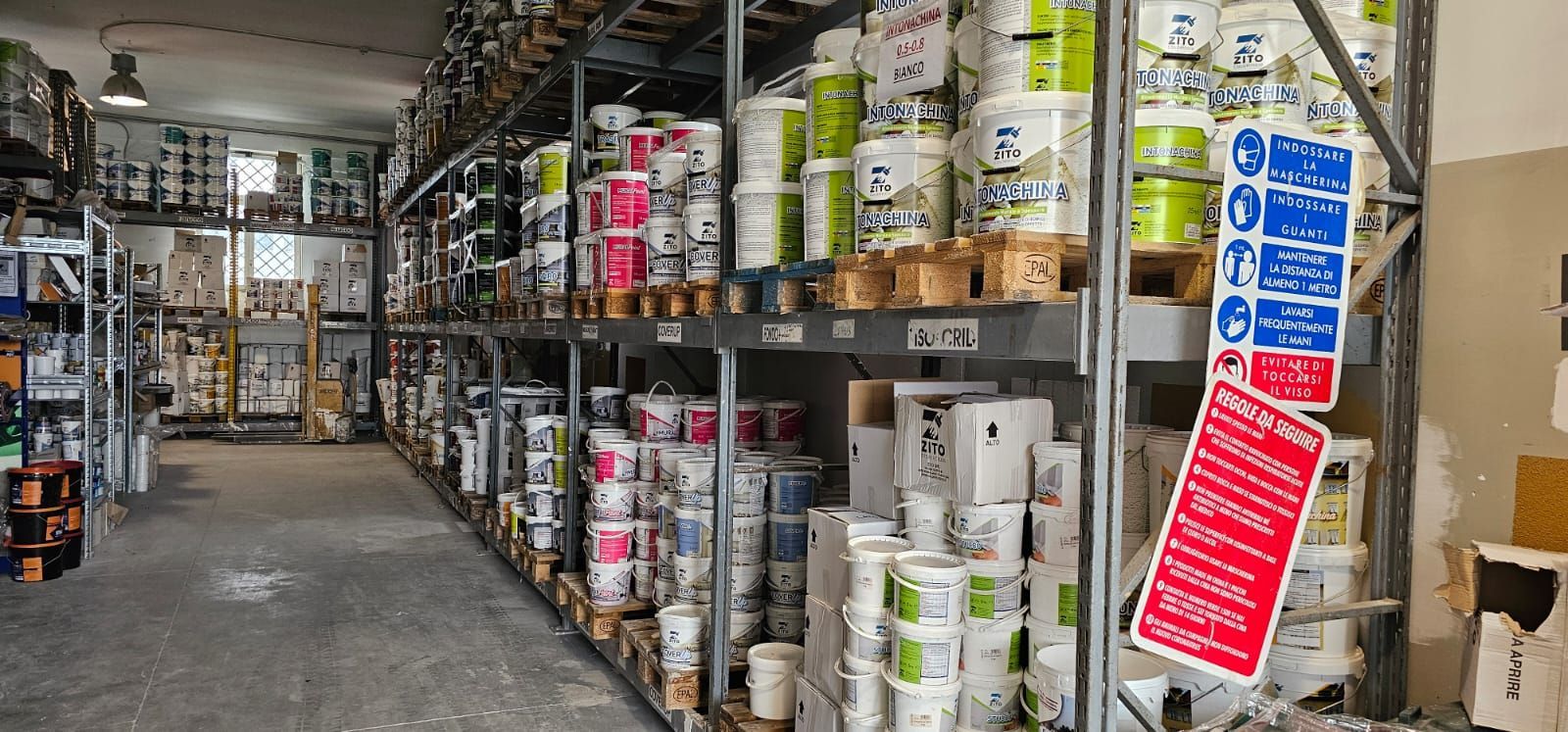 Interno del magazzino con scaffali pieni di barattoli di vernice e cartelli di sicurezza affissi.