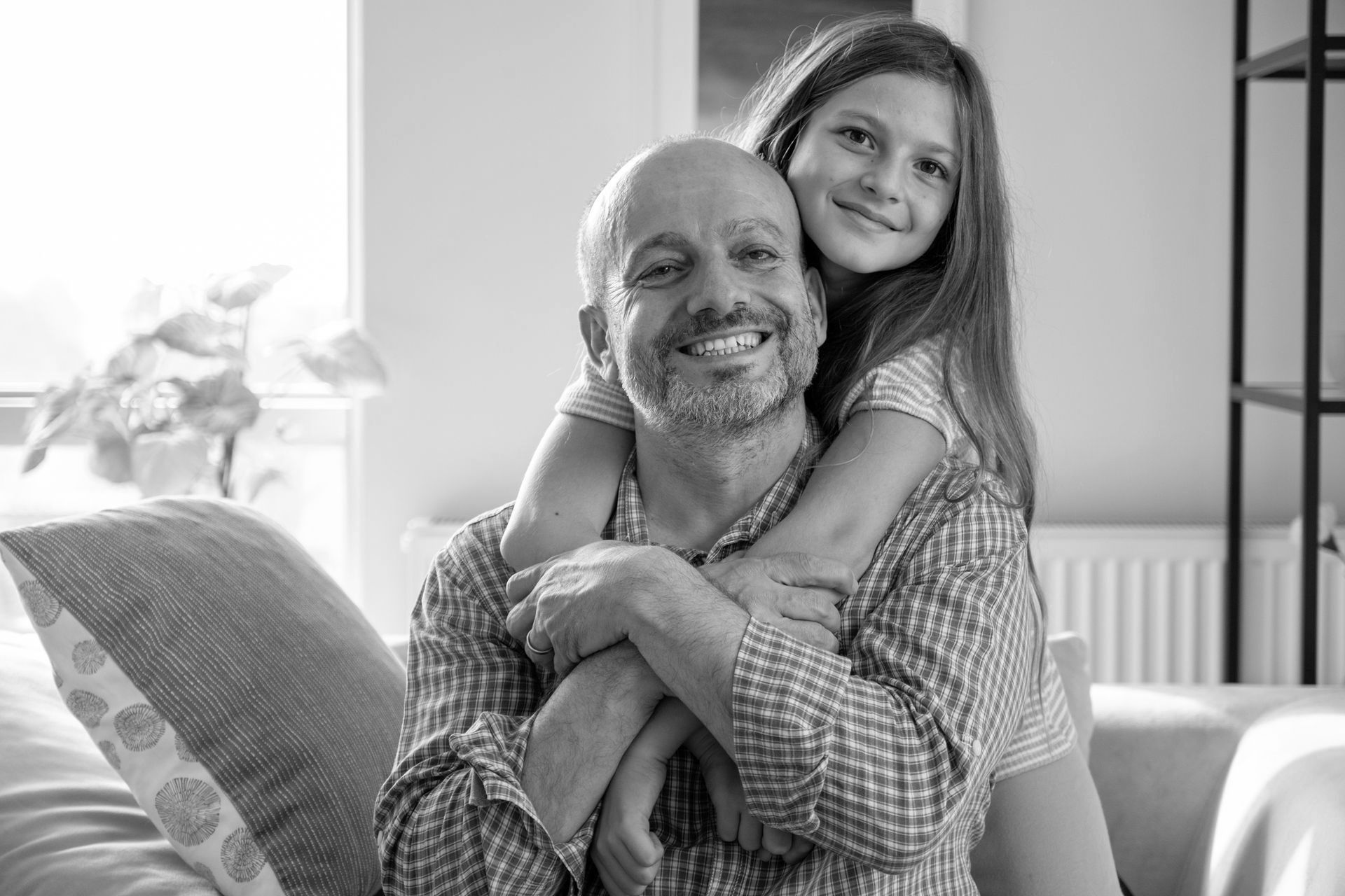 A little girl is hugging a man on a couch.