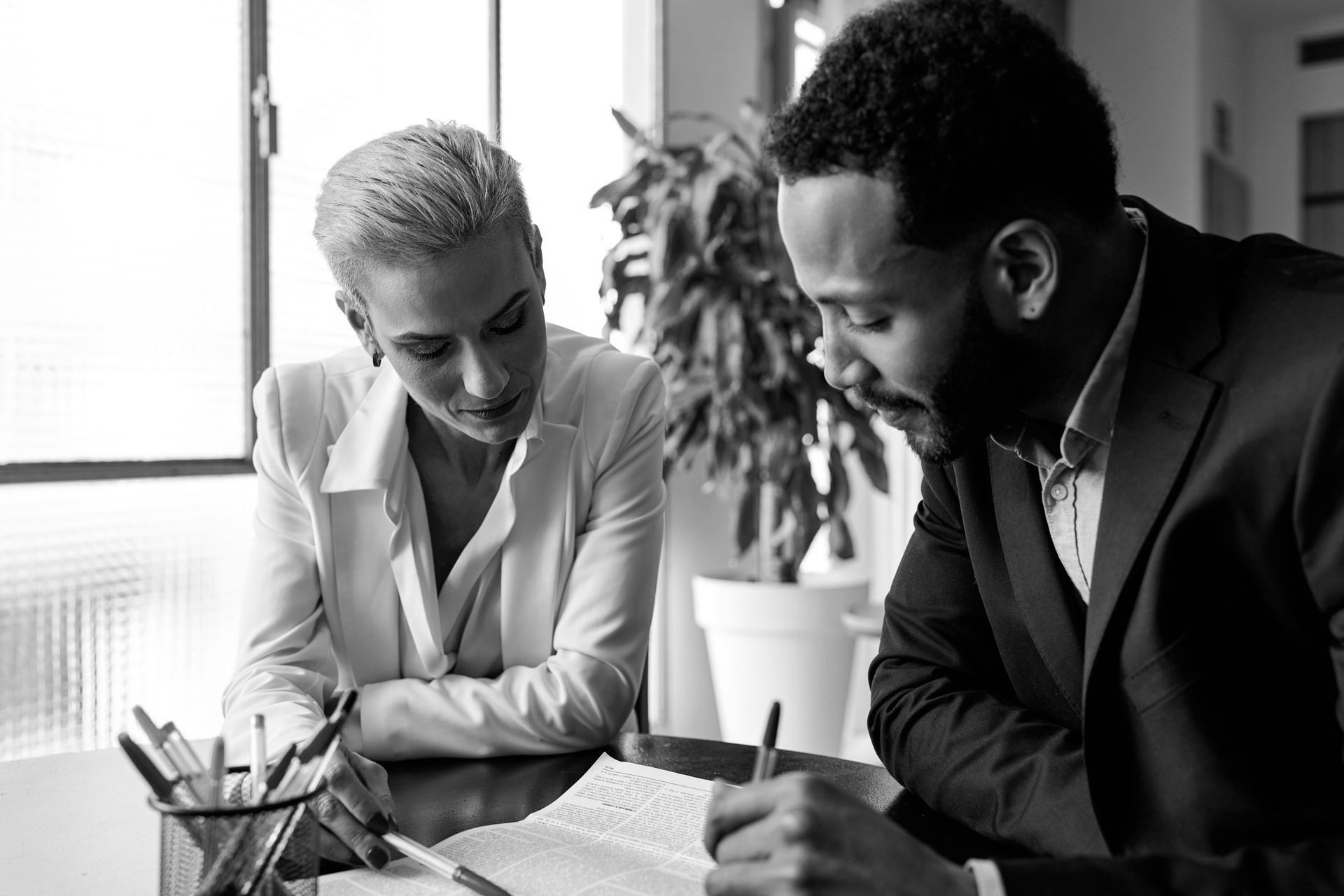 A man and a woman are sitting at a table looking at a book. A man and a woman are sitting at a table looking at a book.