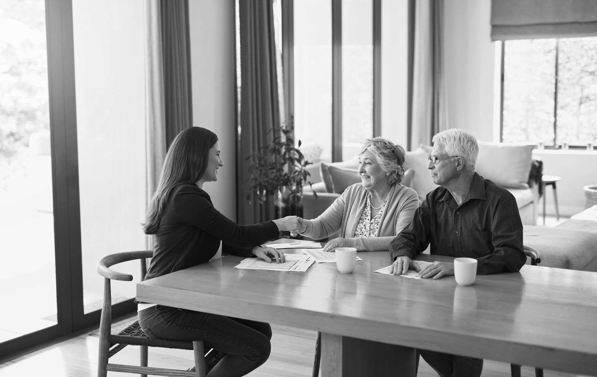 A woman is shaking hands with an elderly couple while sitting at a table. A woman is shaking hands with an elderly couple while sitting at a table.