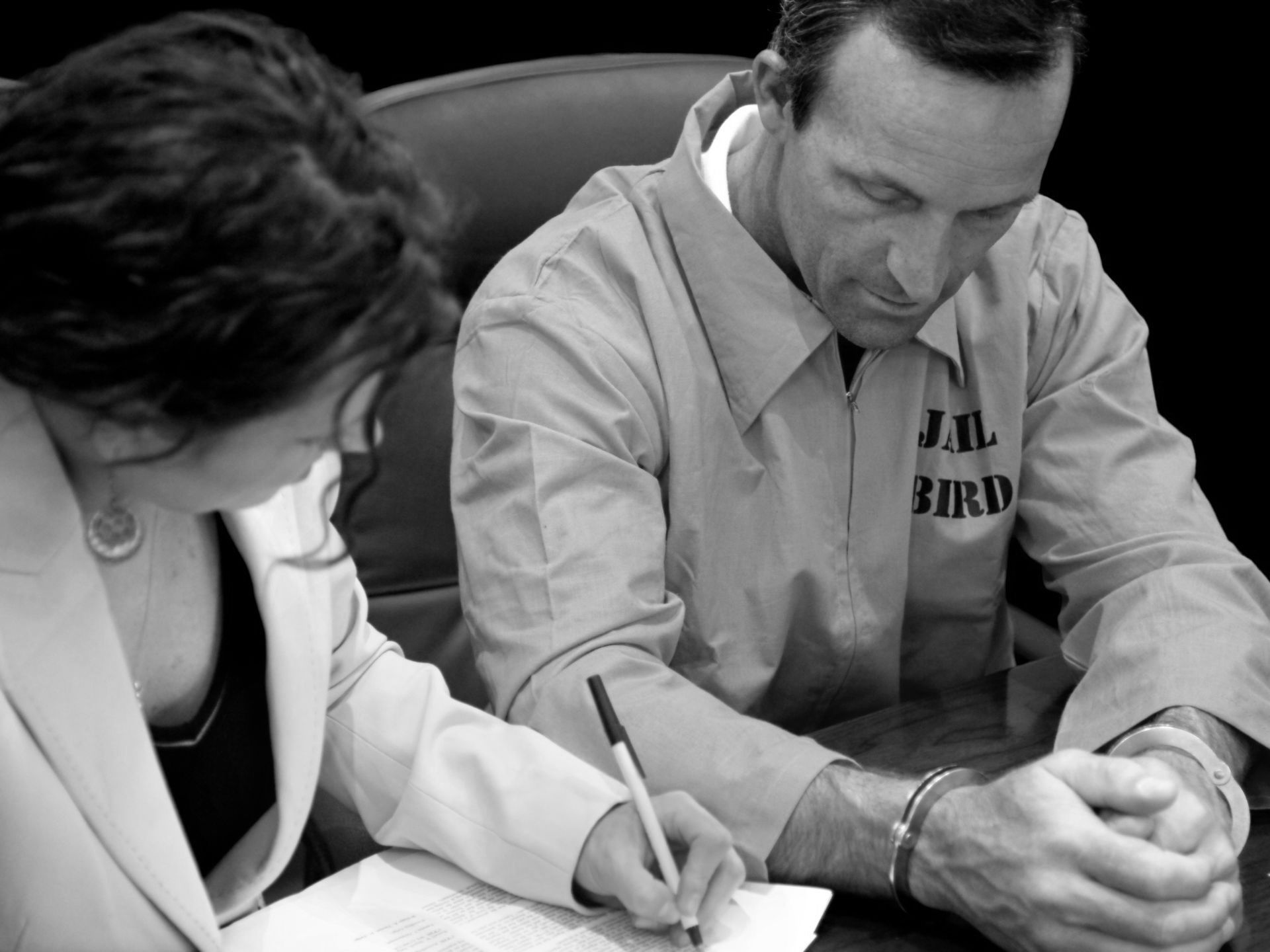 A man in an orange jailbird uniform is signing a document