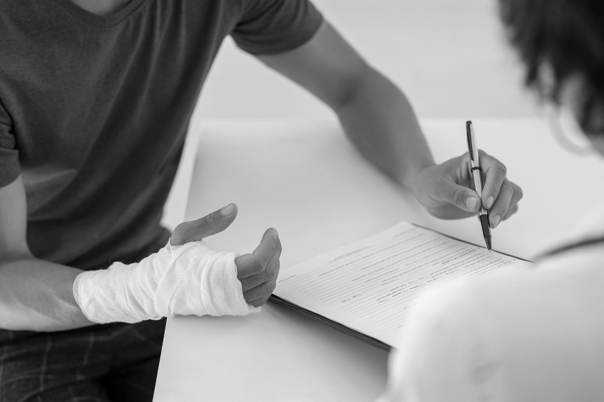 A man with a bandaged hand is sitting at a table talking to a doctor.