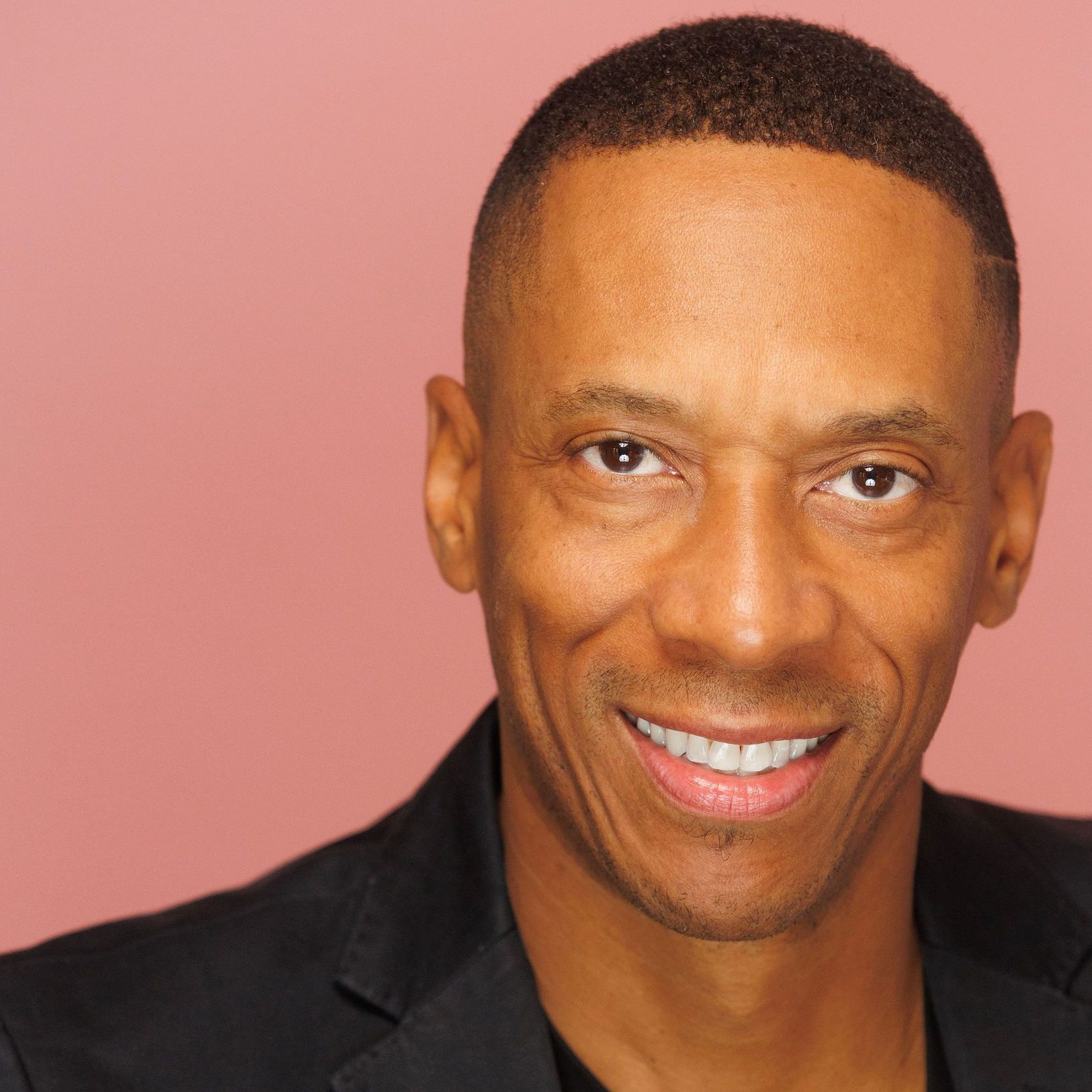 A man in a black suit is smiling for the camera