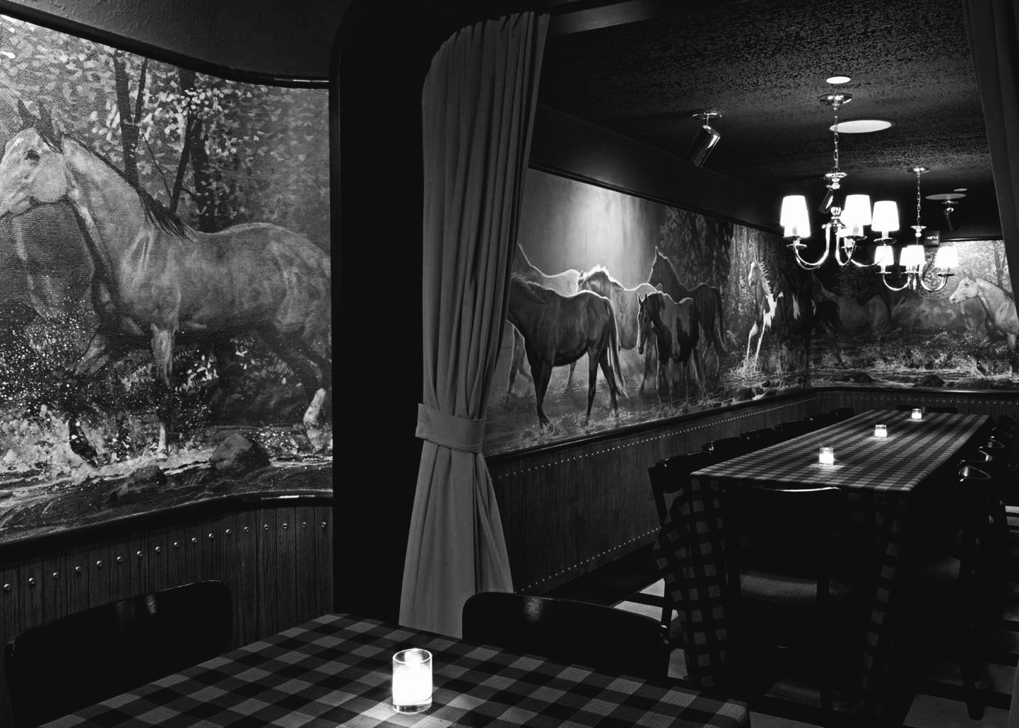black and white photo of a private dining room, on the right a table that seats 14, on the left a mural of a horse. the whole room is decorated with horse motifs.