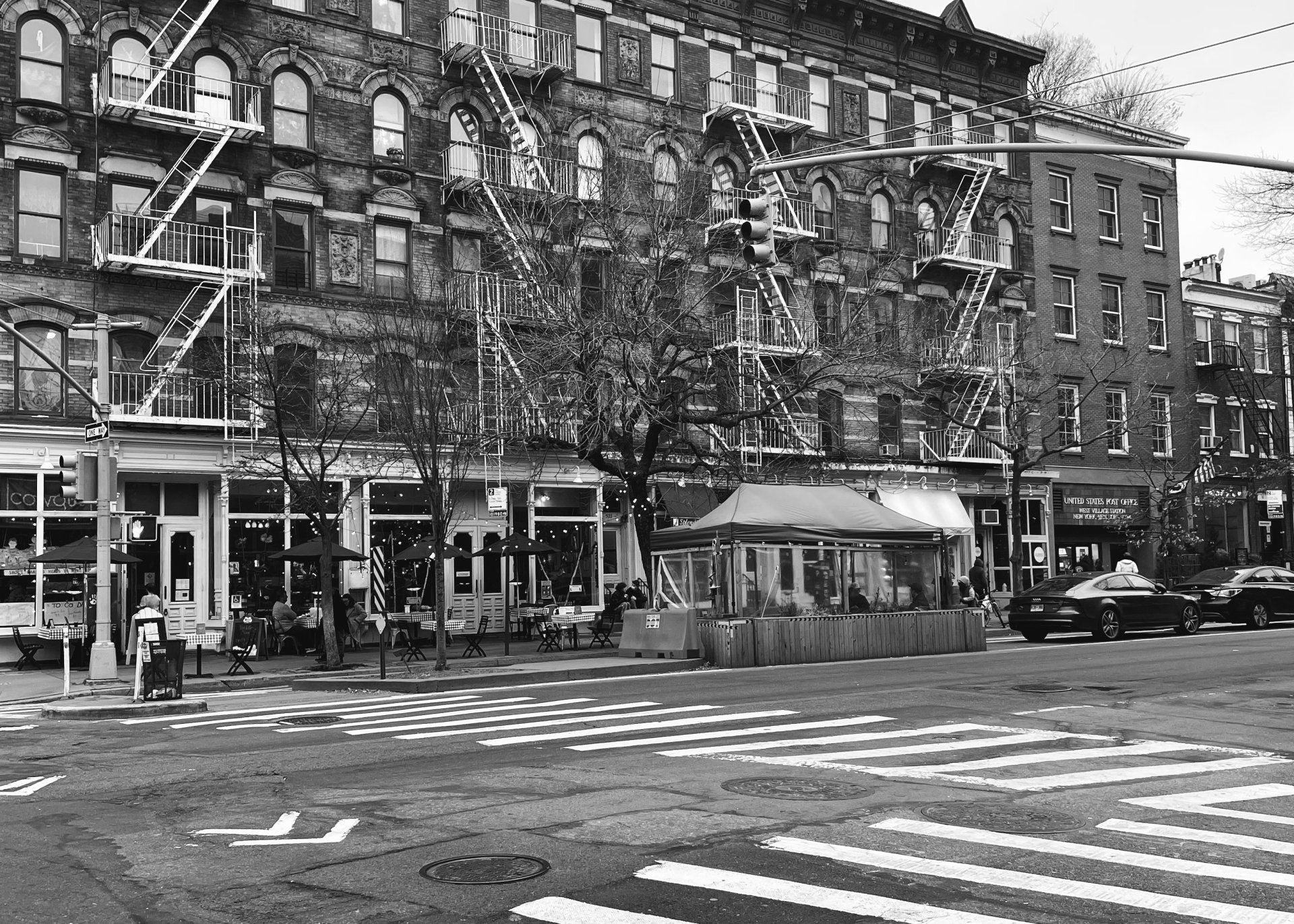 black and white photo of a new york city street, in the backgroun is a post office ans a restaurant
