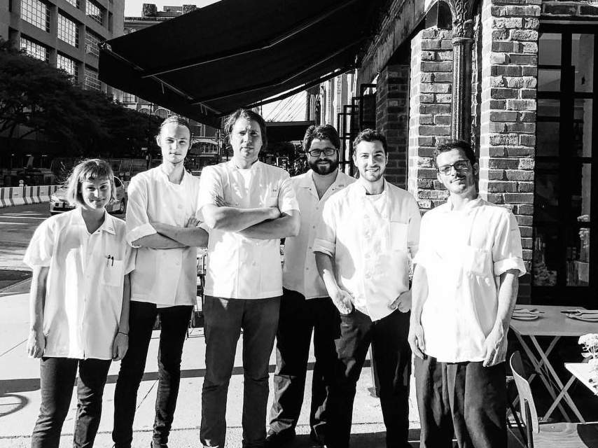 a black and white photo of the restaurant's kitchen team, featuring a female cook, 4 male cooks, and 1 male chef