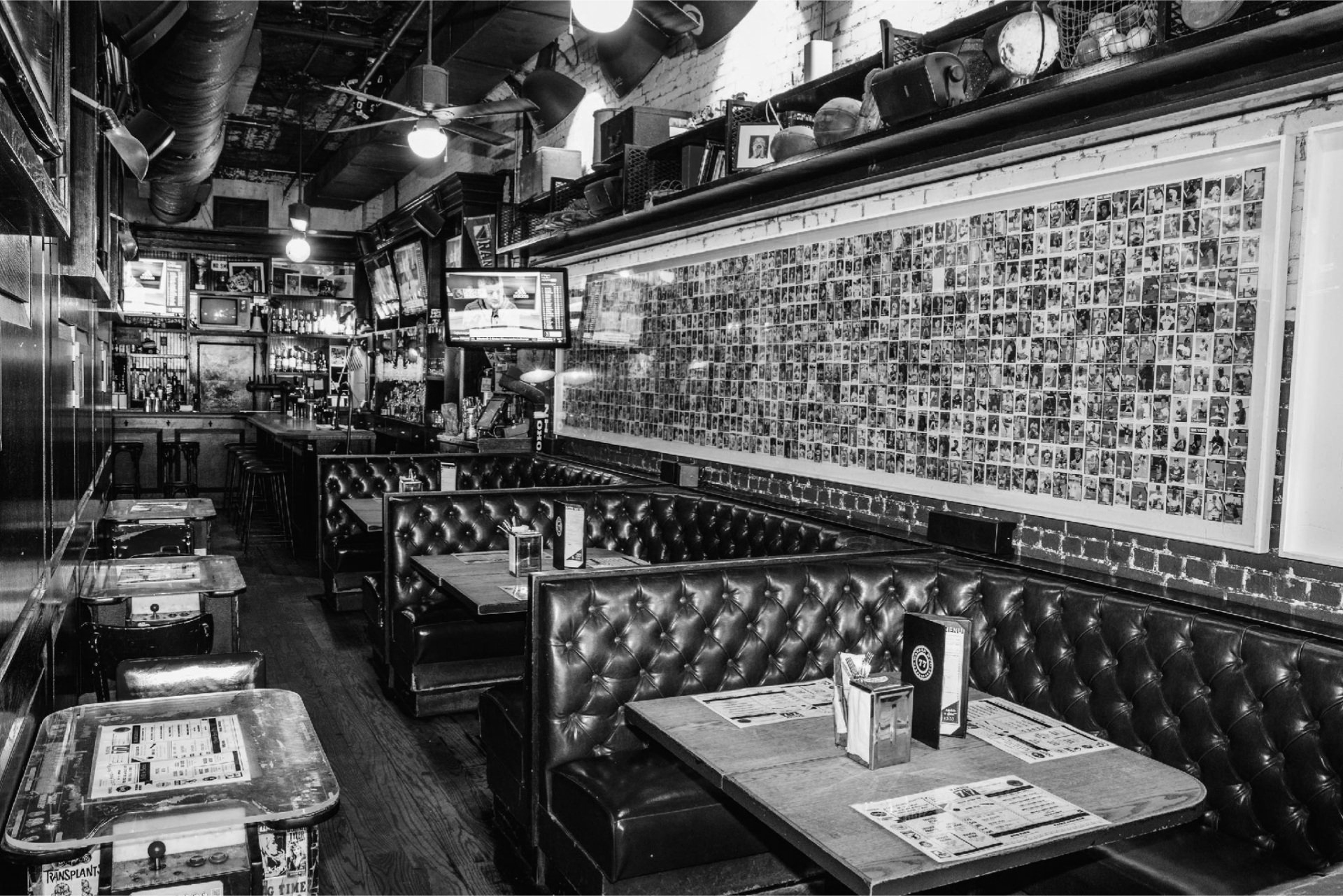 A black and white photo of the bar area of Warren 77, featuring 3 booths, 3 tables, and the bar in the back.