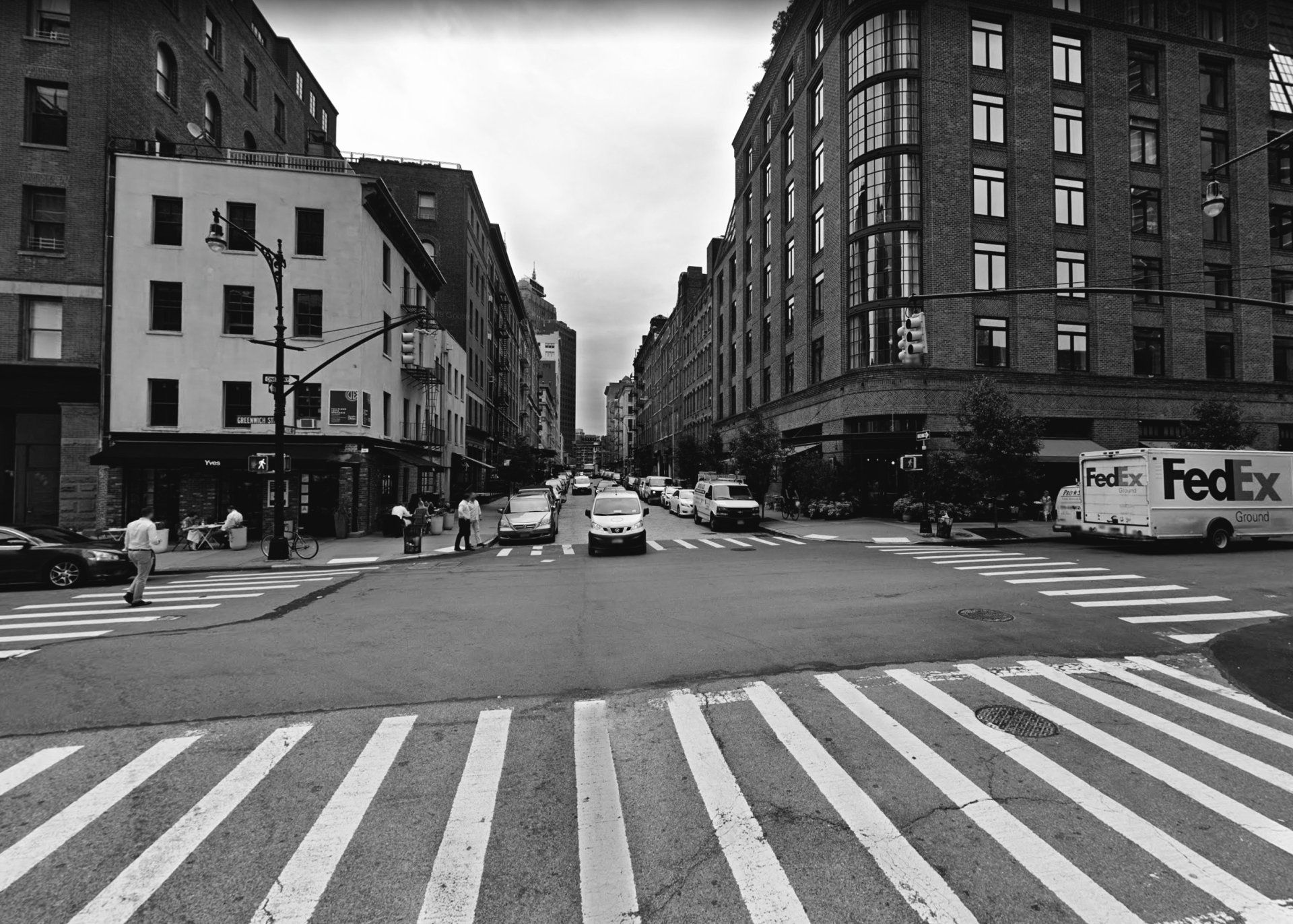 black and white photo of the intersection of  new york city streets with 2 reastaurants, one on each corner.  the restaurant Yves is on the left. On the right another restaurant and a FedEx truck.