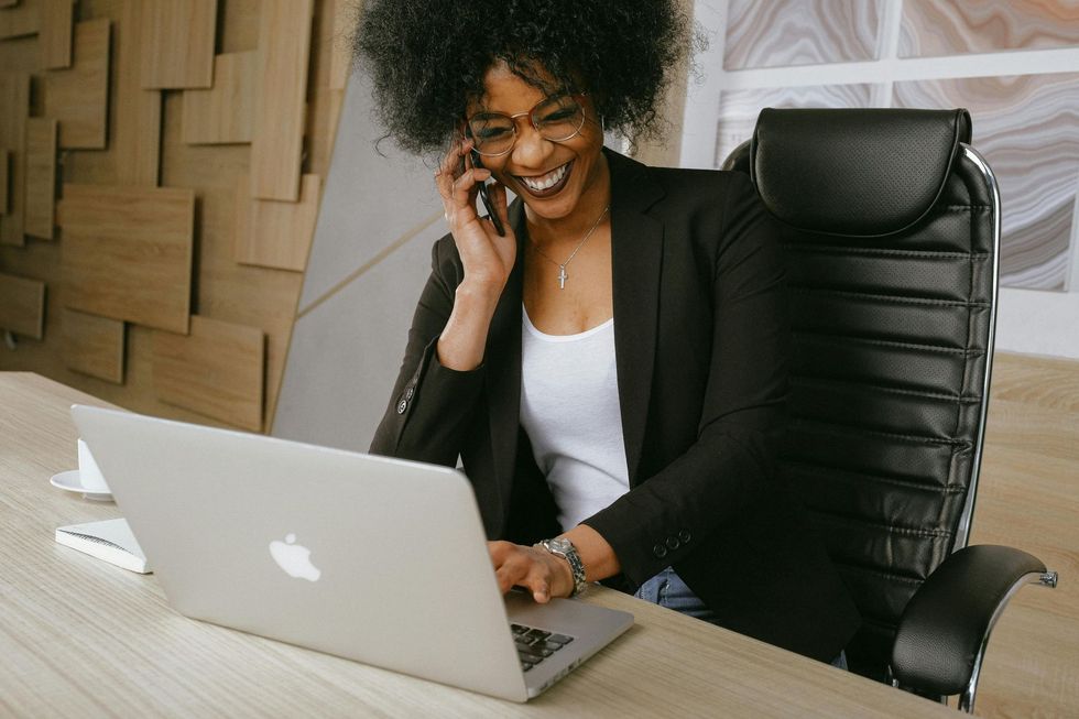 Woman smiling while on phone and using laptop at a desk.