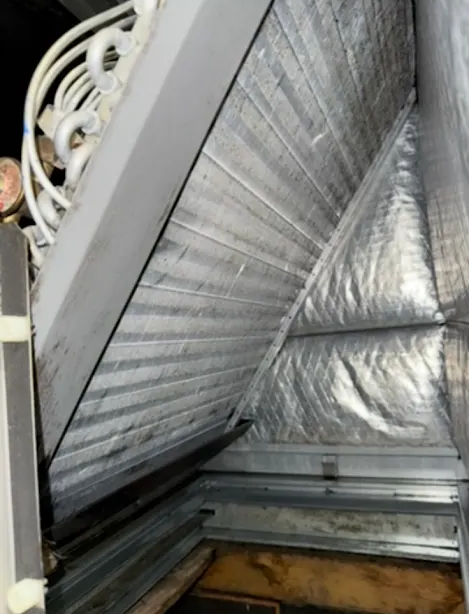 Metal HVAC duct interior with silver insulation and a dark opening in the corner