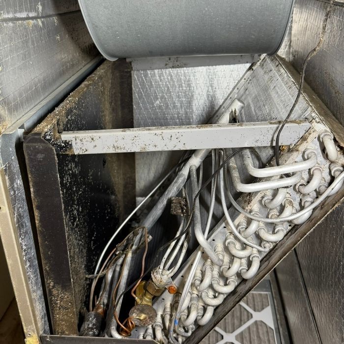 Dirty HVAC unit interior with dusty coils, pipes, and wiring in a metal duct enclosure