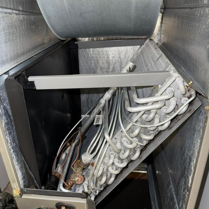 White HVAC coil and wiring inside a metal air handling unit, with insulated ductwork around it