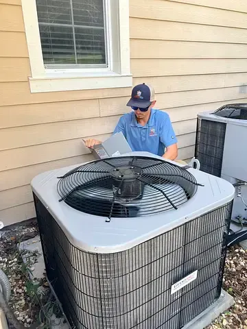 Technician inspecting outdoor air conditioner unit beside a house window