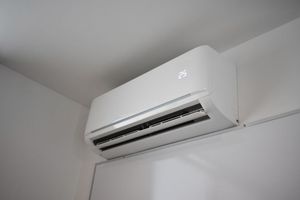 White wall-mounted air conditioner near the ceiling in a plain room