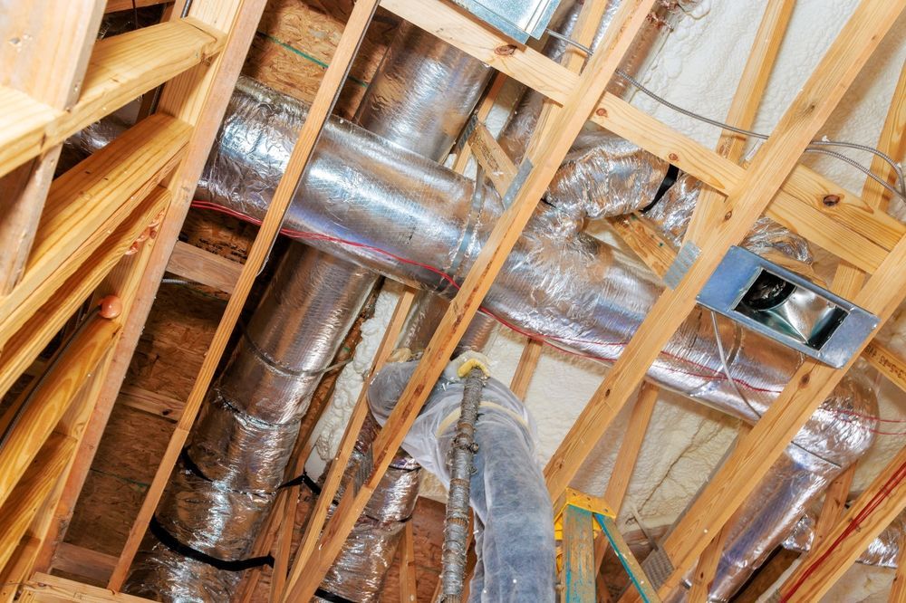 Exposed attic ceiling with wooden rafters, insulation, and silver HVAC ducts viewed from below