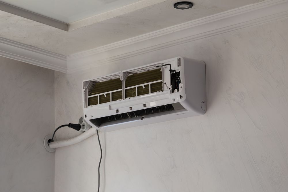 Wall-mounted air conditioner unit with exposed internal components and hanging cables on a white wall