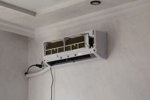 Wall-mounted air conditioner with open front panel and exposed wiring in a white room