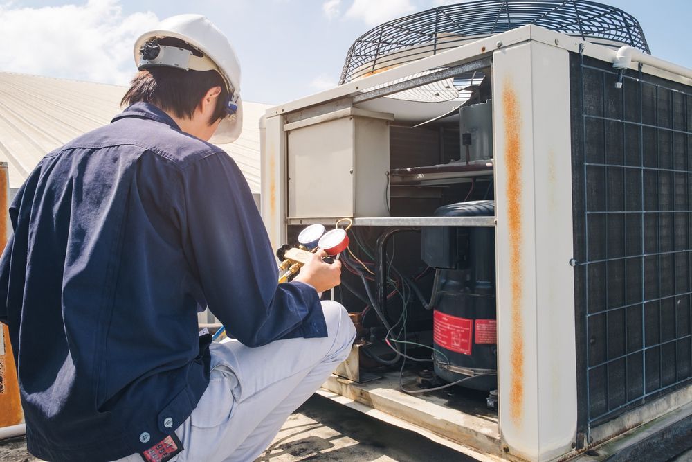 Technician inspecting an open rooftop HVAC unit with tools on a sunny day