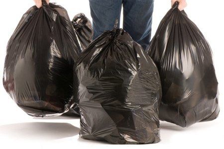 Una persona sostiene tres bolsas de basura negras en sus manos.