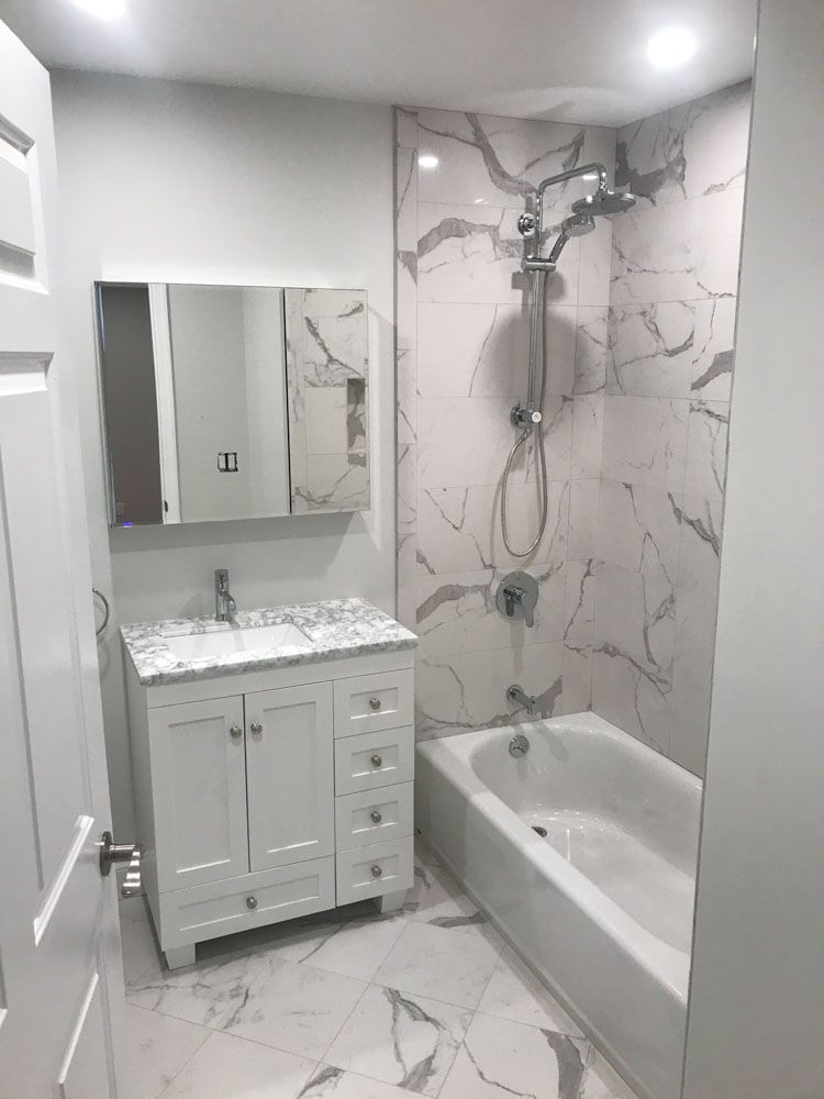 White bathroom with marble-look tile, vanity, tub, and showerhead.