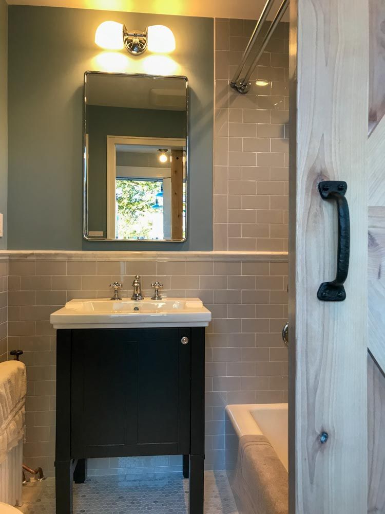 Bathroom with vanity, mirror, and tiled wall; light blue walls, gray tile, and a partially open wooden door.