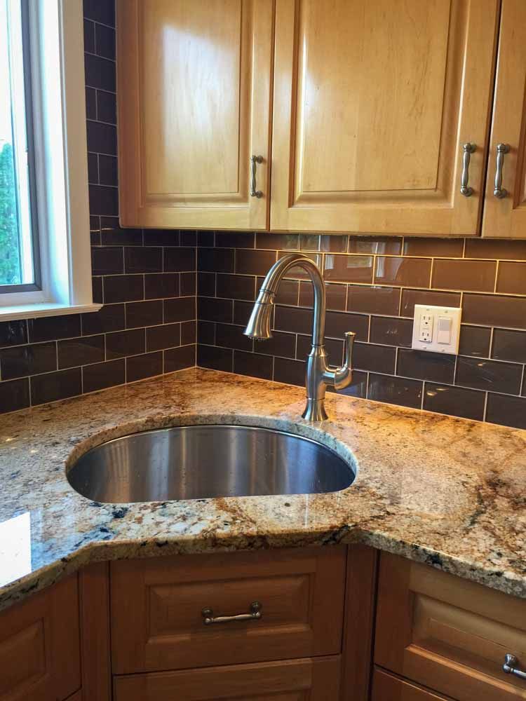 Kitchen corner with stainless steel sink, granite countertop, and brown tile backsplash.