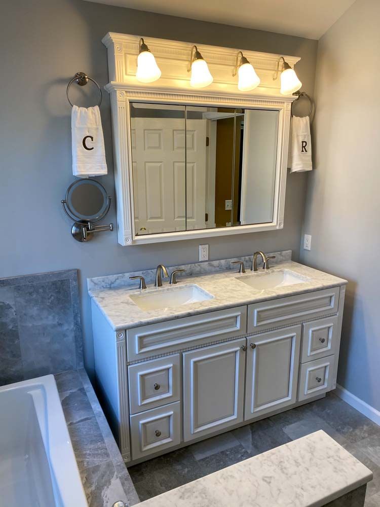 Bathroom vanity with double sinks, marble countertop, gray cabinets, mirror, and overhead lights.