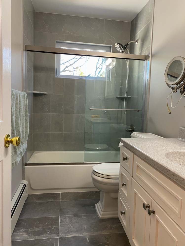 Bathroom with a white tub and toilet, gray tile walls and floor, and a white vanity.