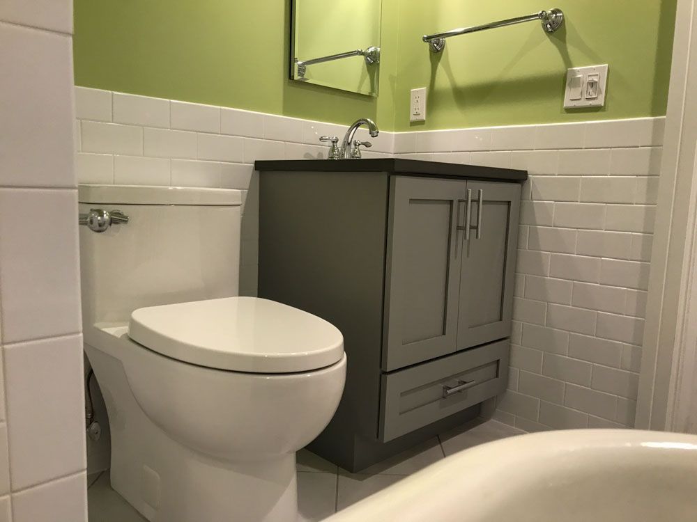 Bathroom with gray vanity, white toilet, light green wall, and white tile.