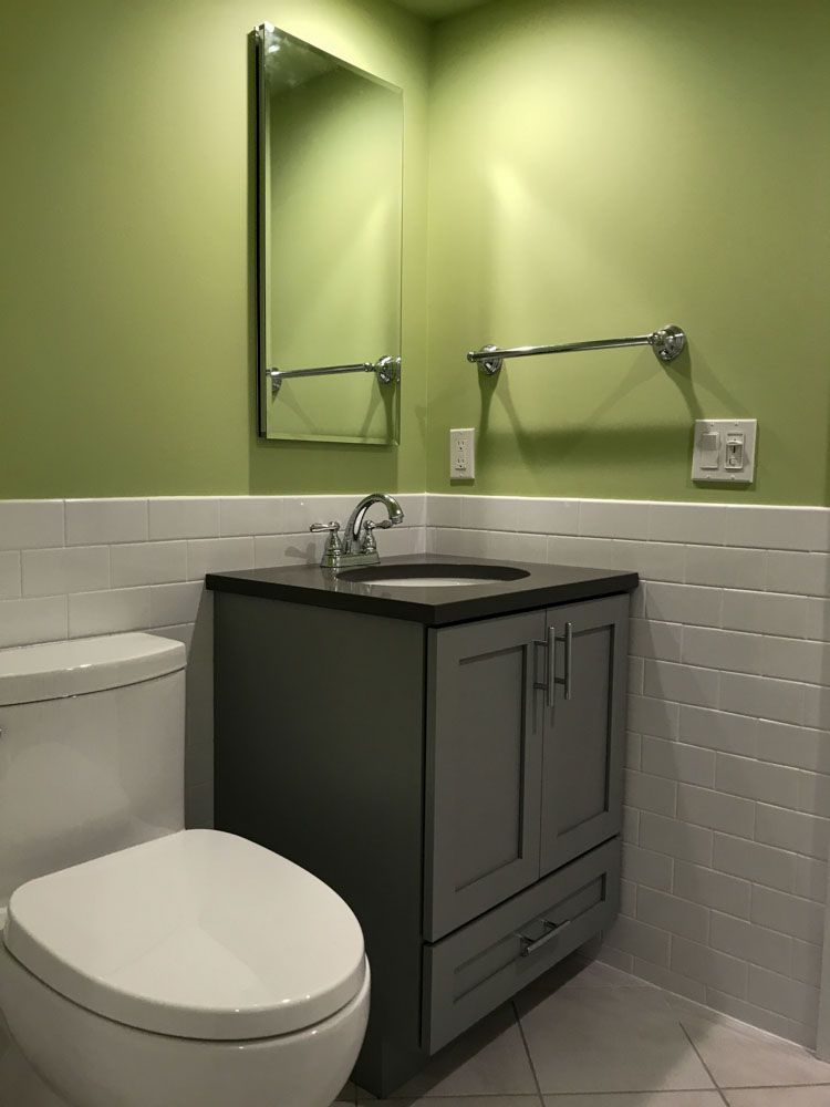 A small bathroom with a green wall, gray vanity, toilet, and white tiled lower walls.