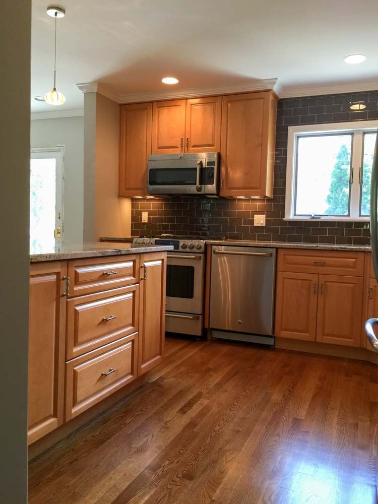 Kitchen with wood cabinets, stainless steel appliances, and dark tiled backsplash; hardwood floor.
