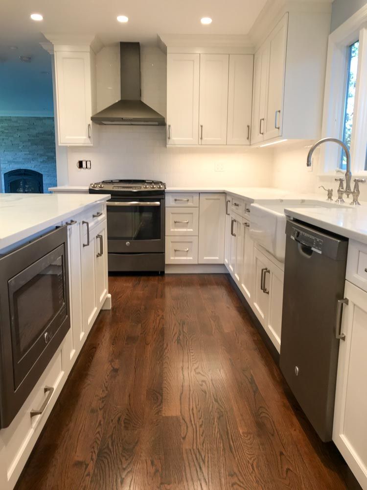 White kitchen with dark wood floors, stainless appliances, and white countertops.