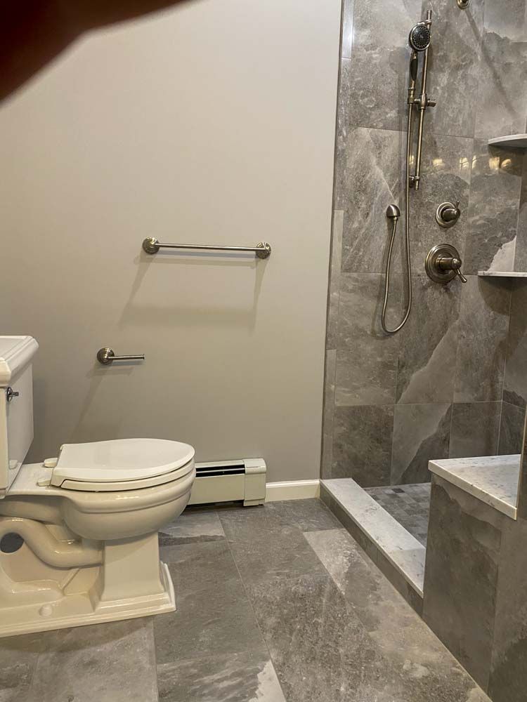 Bathroom with toilet, shower, gray tile, and grab bars.