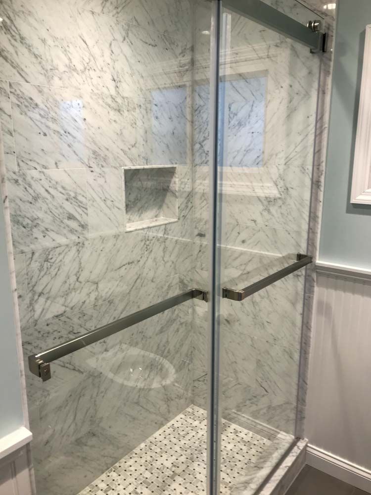 Shower with marble walls and a glass door, featuring grab bars.