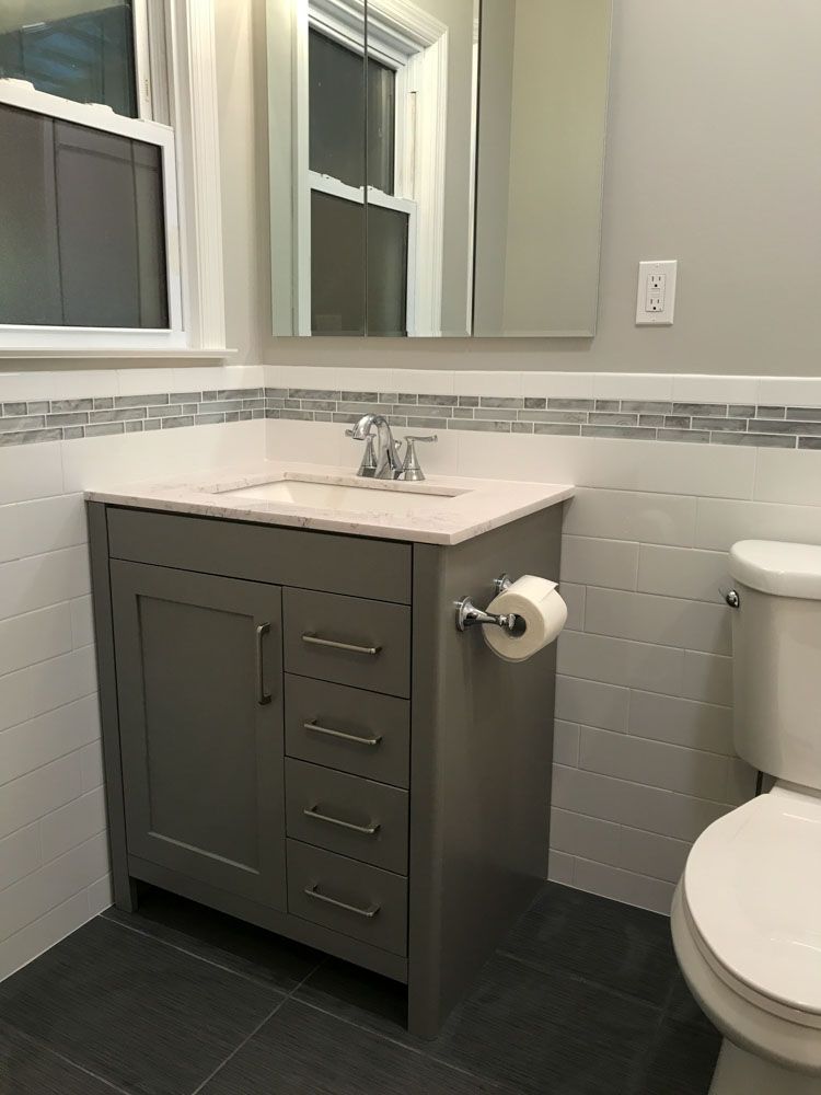 Gray vanity in a bathroom with a white countertop, white and gray tile, and a toilet.