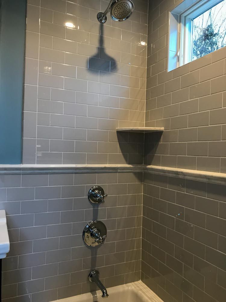 Gray tiled shower with showerhead, faucet, and built-in shelf. Window provides natural light.
