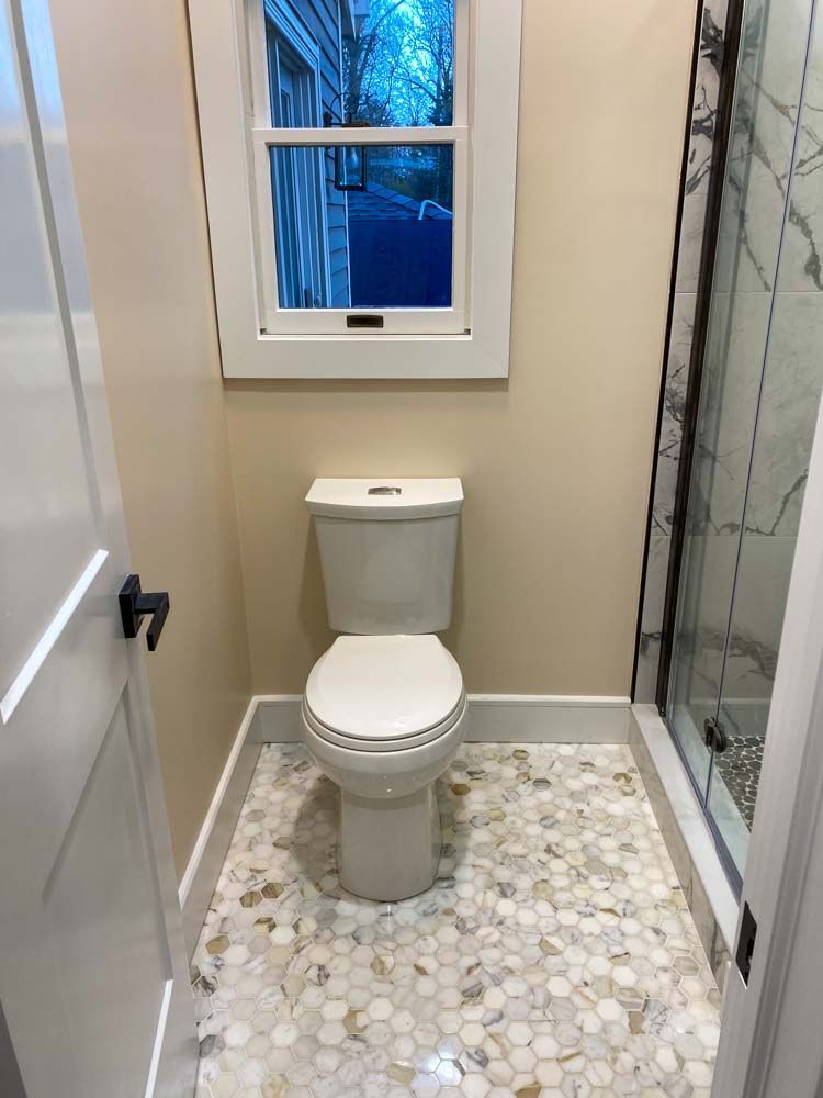 Small bathroom with a toilet, window, and pebble tile floor.