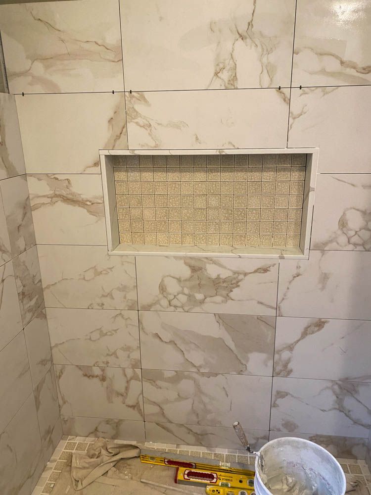 Shower with marble-like tiles; a niche is tiled with small squares. Tools and mortar bucket at the bottom.