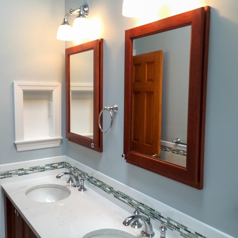 Bathroom with two sinks, mirrors reflecting a door, and a recessed shelf; light blue walls.