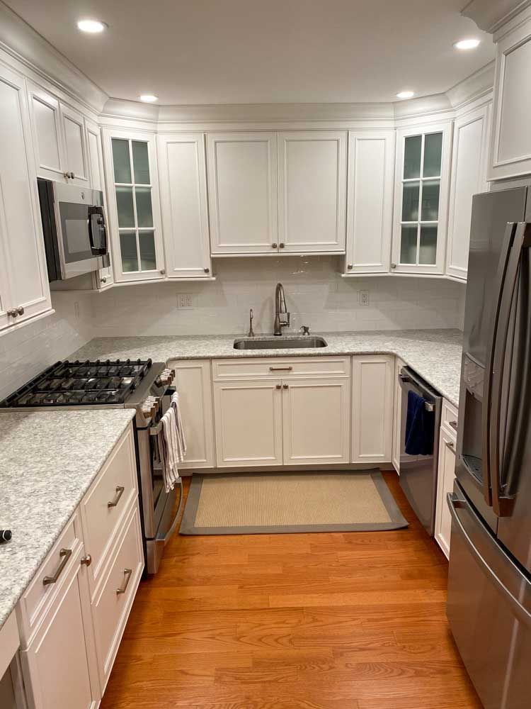 White kitchen with stainless steel appliances, light countertops, and wood floors.
