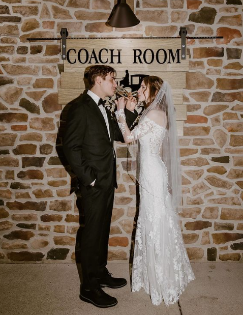 A bride and groom are drinking champagne in front of The Coach Room sign.