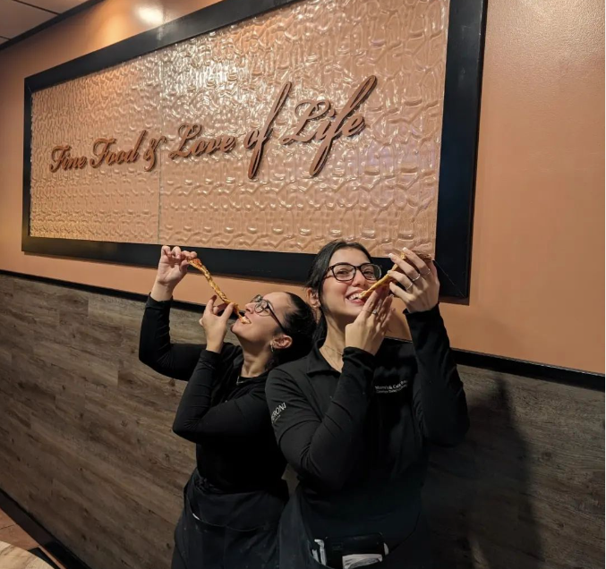 Two women eating pizza in front of a sign that says 