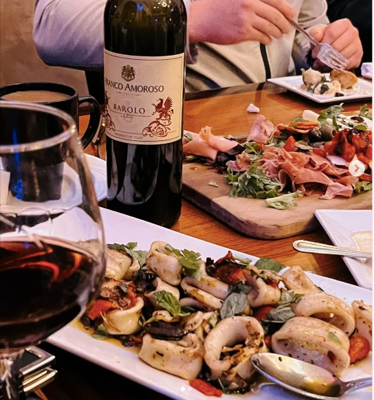 A bottle of carlo amoroso wine sits on a table next to a plate of food at Mama’s Cafe Baci