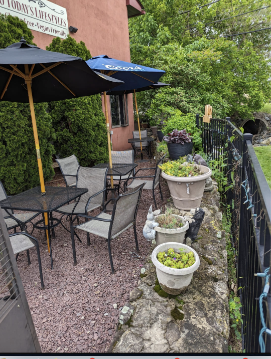 A patio with tables , chairs , umbrellas and potted plants.
