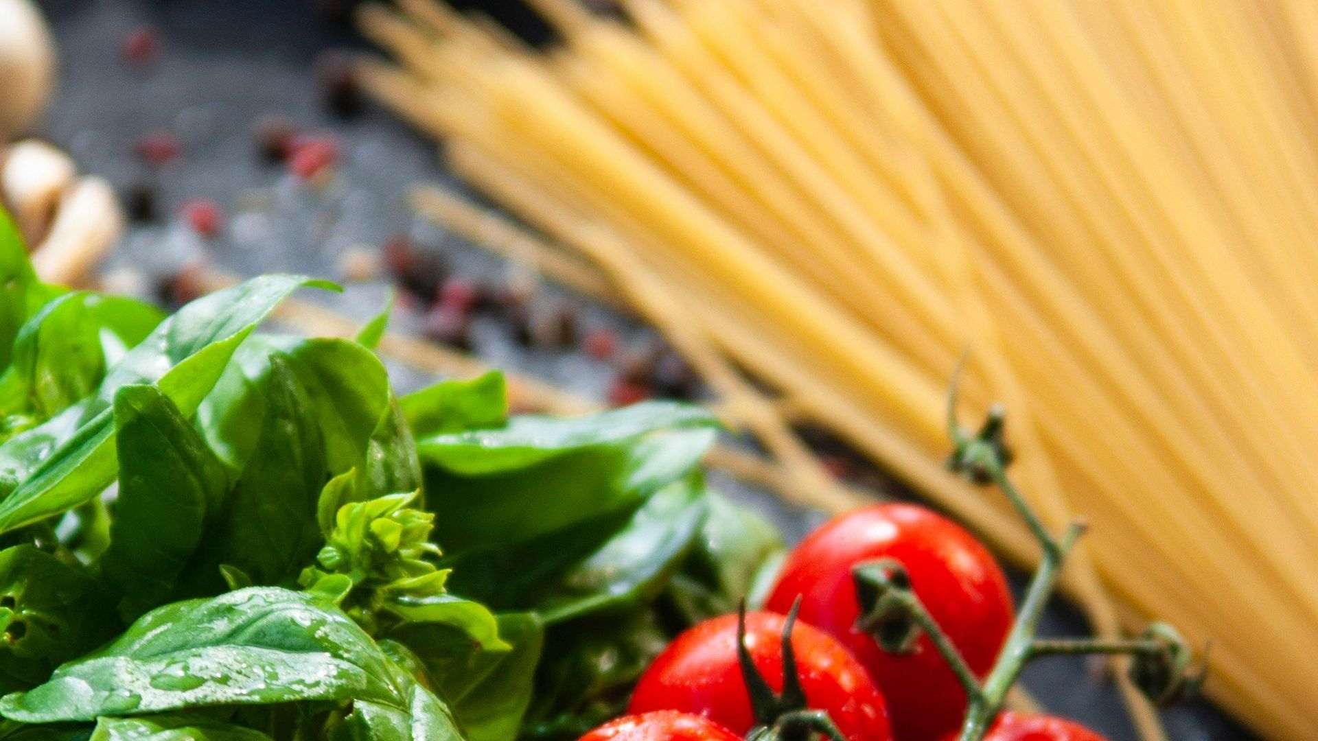 A close up of tomatoes , basil , spaghetti and other vegetables on a table.