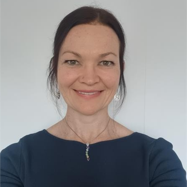 A woman with blonde hair is smiling and praying on the beach.
