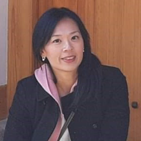 A woman wearing a black jacket and a pink scarf is sitting in front of a wooden door.